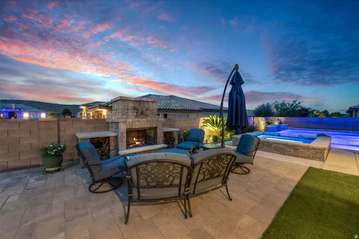 Expansive outdoor living area featuring a stone-clad fireplace, integrated hot tub, and swimming pool with blue lighting