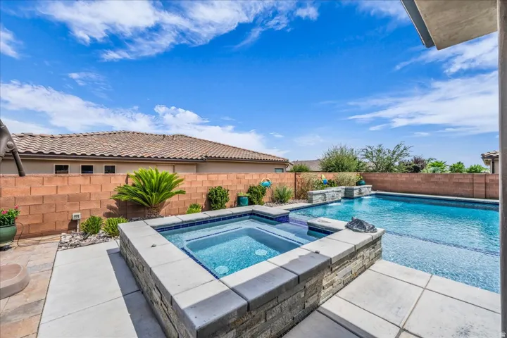 Swimming pool with integrated spa and stone-clad waterfall features, surrounded by concrete and paver patios