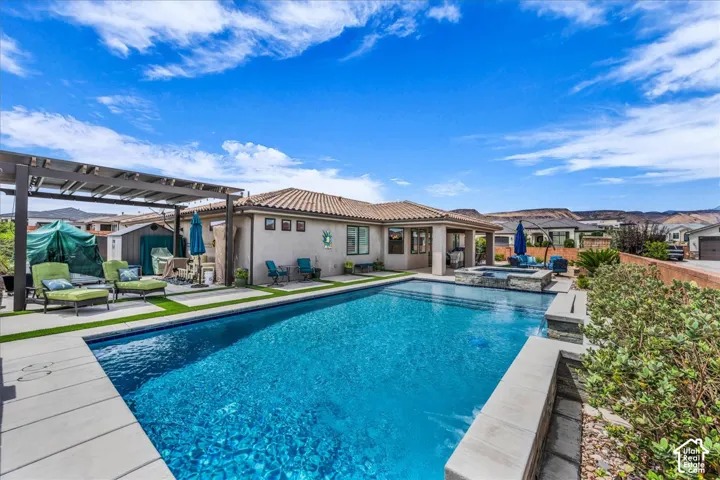 Expansive backyard featuring a rectangular swimming pool, integrated spa, pergola, and lush landscaping
