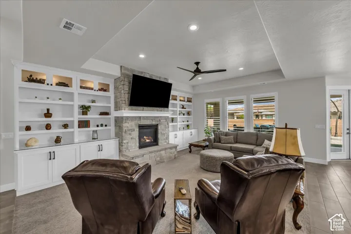 Stone surround fireplace with built-in cabinetry, tray ceiling, recessed lighting, and wood-finish flooring