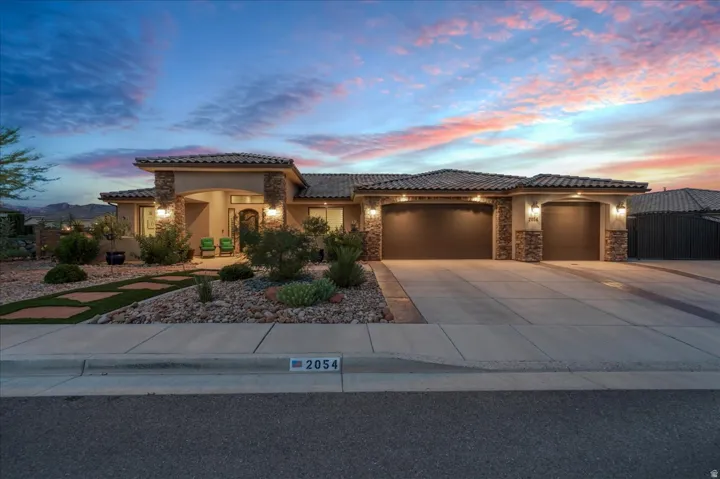Stucco exterior with stone accents, tile roof, multi-car driveway, and integrated outdoor lighting