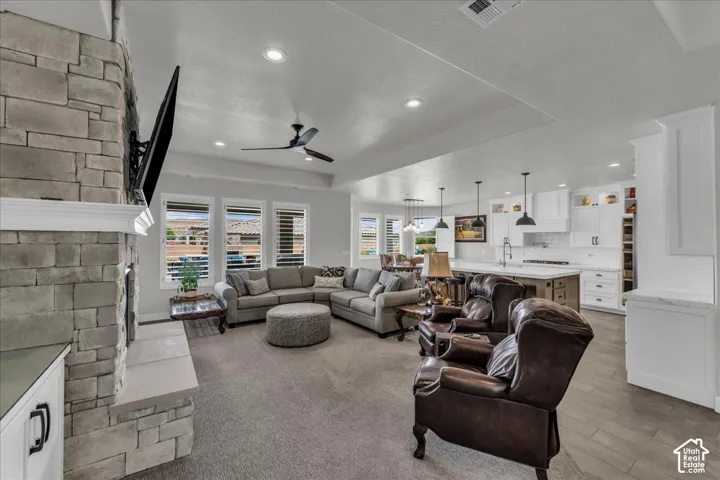 Stone-clad fireplace with mantel, recessed lighting, ceiling fan, white kitchen cabinetry, and pendant lighting