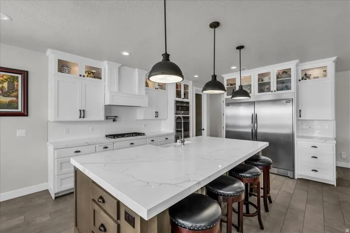 Expansive kitchen island with a quartz countertop, white shaker cabinetry, stainless steel appliances, and wood-finish flooring