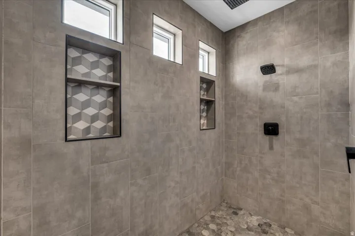Spa-inspired shower featuring large-format gray tile walls, recessed shelving with geometric tile accent, skylight windows for natural illumination, and dual wall-mounted fixtures