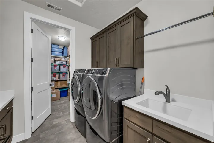 Laundry room featuring wood-finish cabinetry, solid surface countertop with integrated sink, and a hanging rod