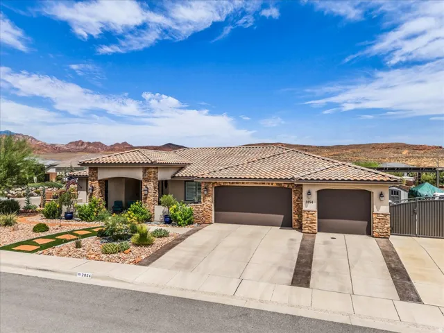 Mediterranean-style exterior with a tile roof, stone accents, two-car garage, and desert landscaping
