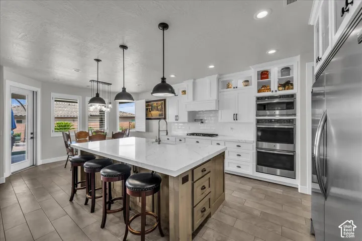 White shaker cabinetry, stainless steel appliances, central island with seating, pendant lighting, and wood-finish flooring