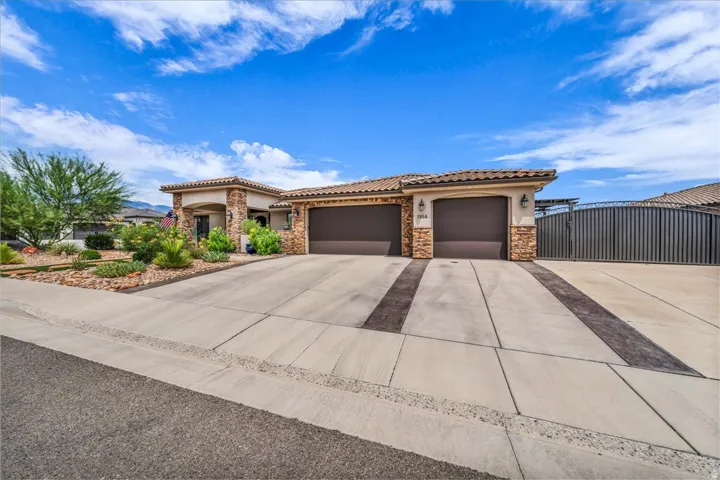 Stucco exterior featuring stone accents, a tile roof, an integrated two-car garage, and a large concrete driveway with decorative banding