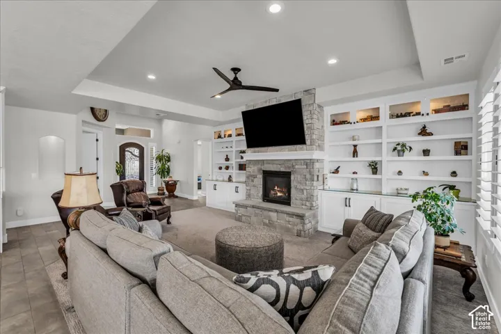 Living area featuring a stone fireplace, integrated built-in shelving, tray ceiling, recessed lighting, and a ceiling fan