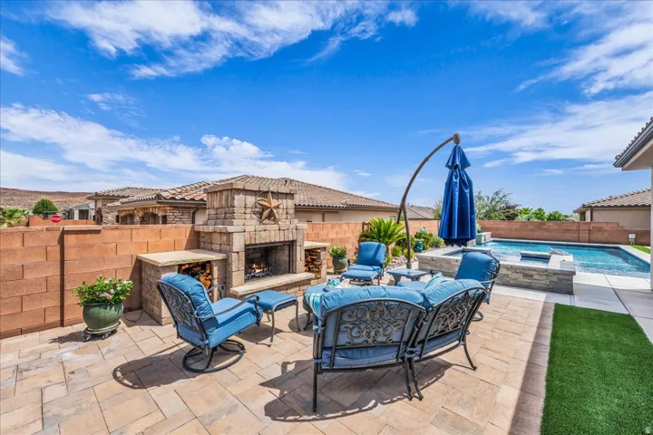 Paved patio featuring a stone fireplace, built-in outdoor kitchen elements, a swimming pool, and a spa