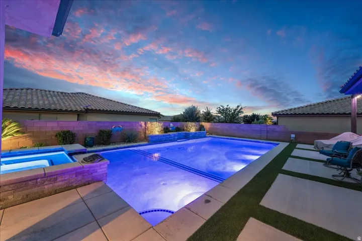 Outdoor living area featuring a custom pool, integrated spa, paver patio, and low-maintenance artificial turf accents