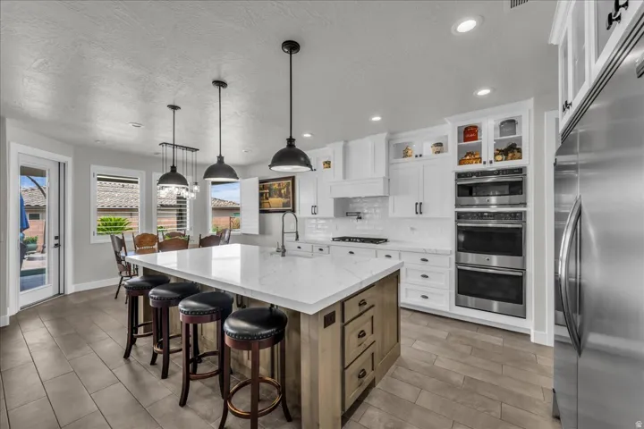 White shaker cabinetry, stainless steel appliances, central island with seating, pendant lighting, and wood-finish flooring