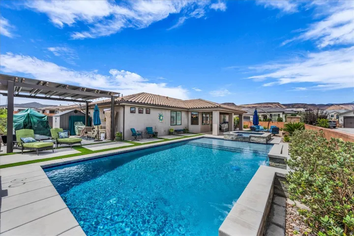 Expansive backyard featuring a rectangular swimming pool, integrated spa, pergola, and lush landscaping