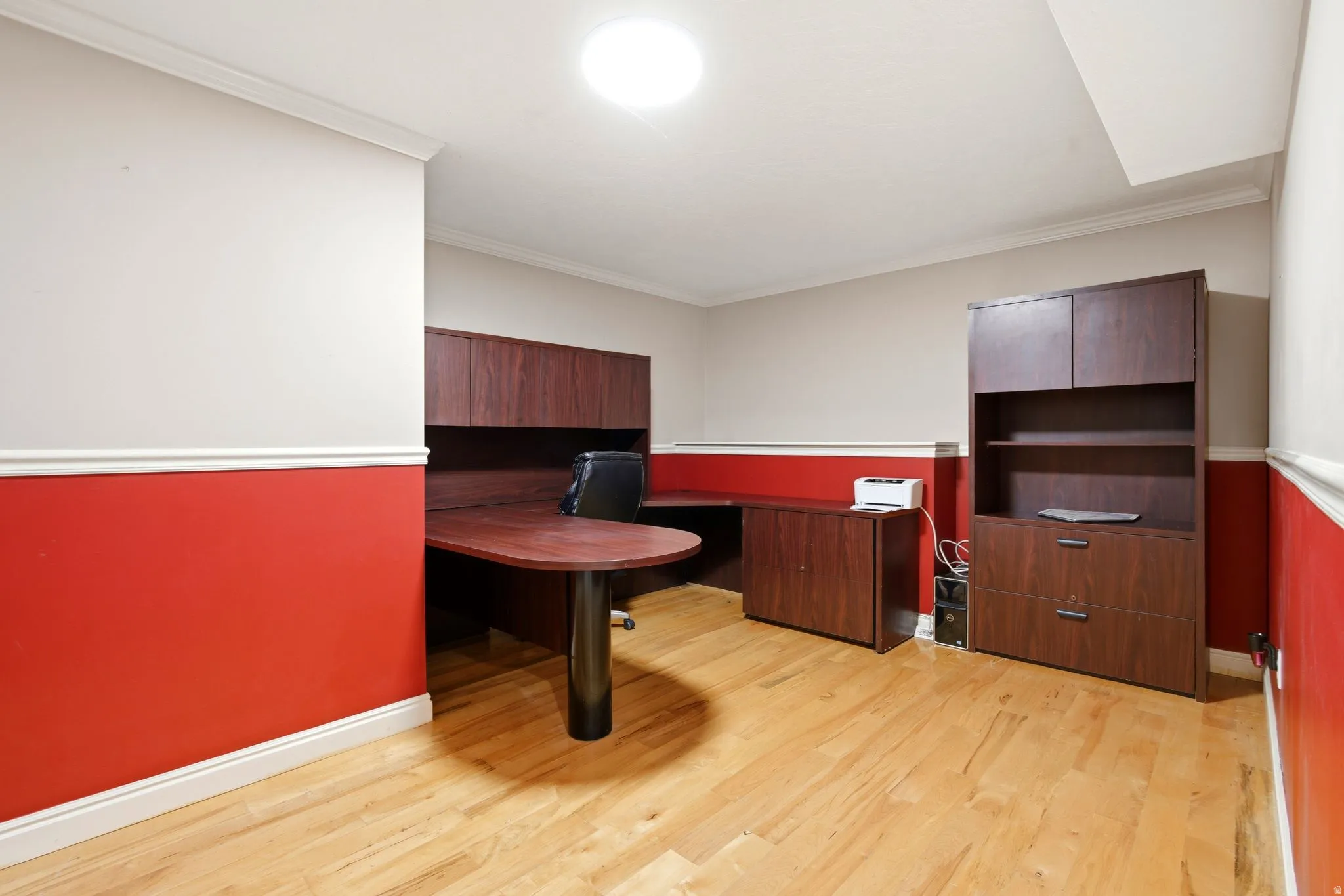 Professional office suite featuring rich wood-finish cabinetry and built-in storage, warm wood-finish flooring, bold red accent walls with crisp white trim, and recessed ceiling lighting throughout the space