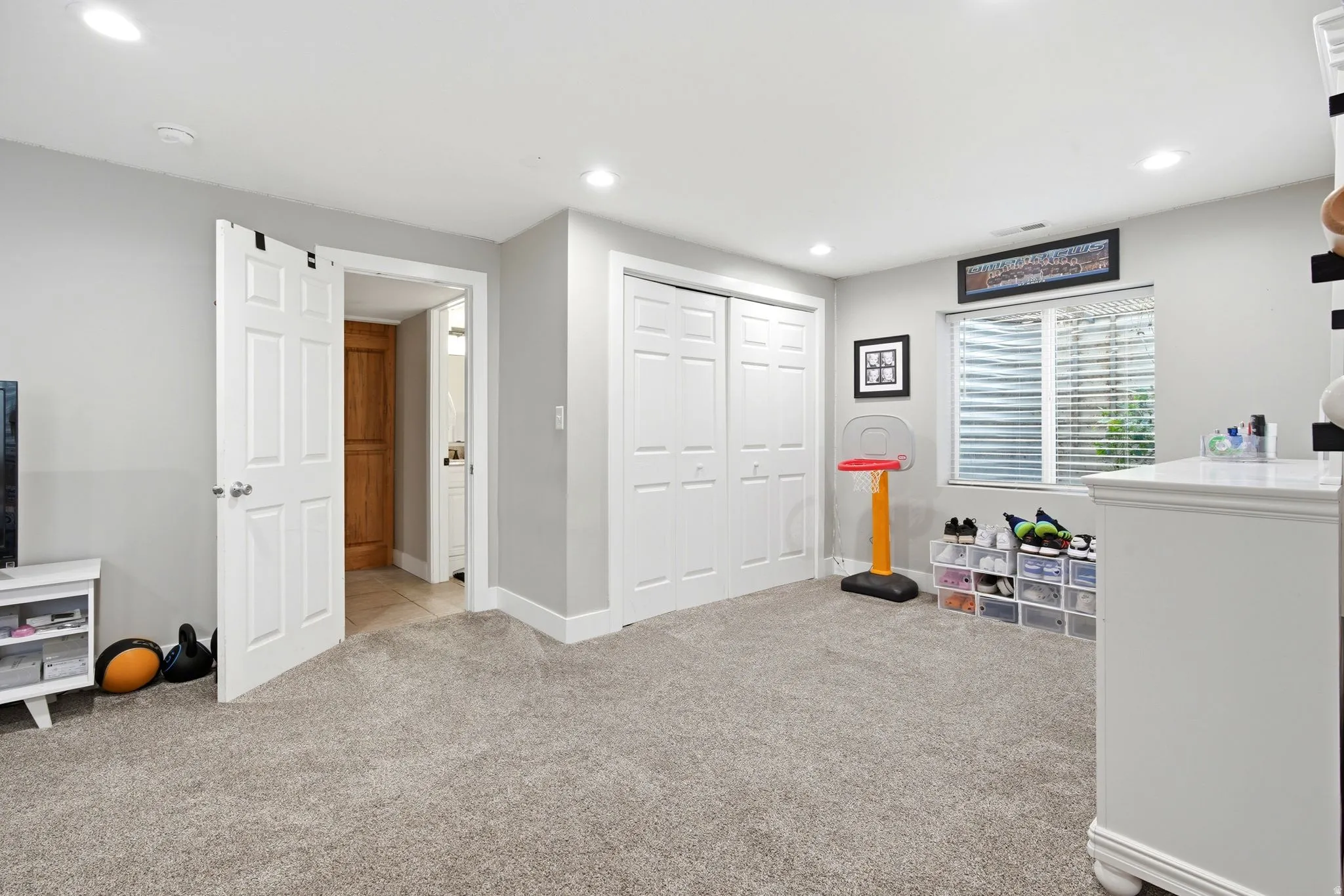 Spacious bedroom with neutral carpeting, abundant natural light from multiple windows with plantation shutters, double closet doors with white six-panel design, and recessed ceiling lighting throughout