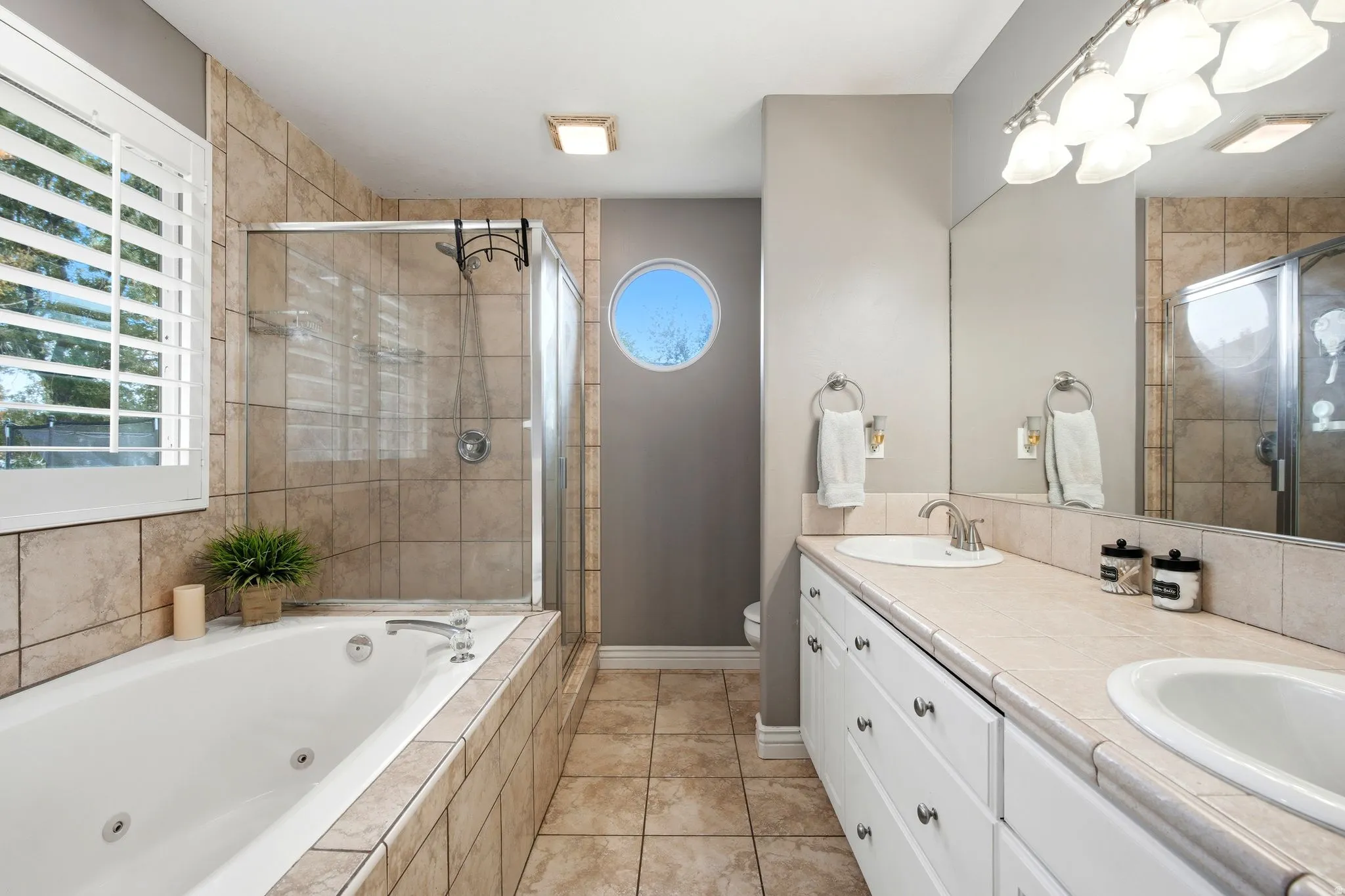 Spa-inspired primary bathroom showcasing dual vanities with white cabinetry and brushed nickel hardware, ceramic vessel sinks, and a large framed mirror