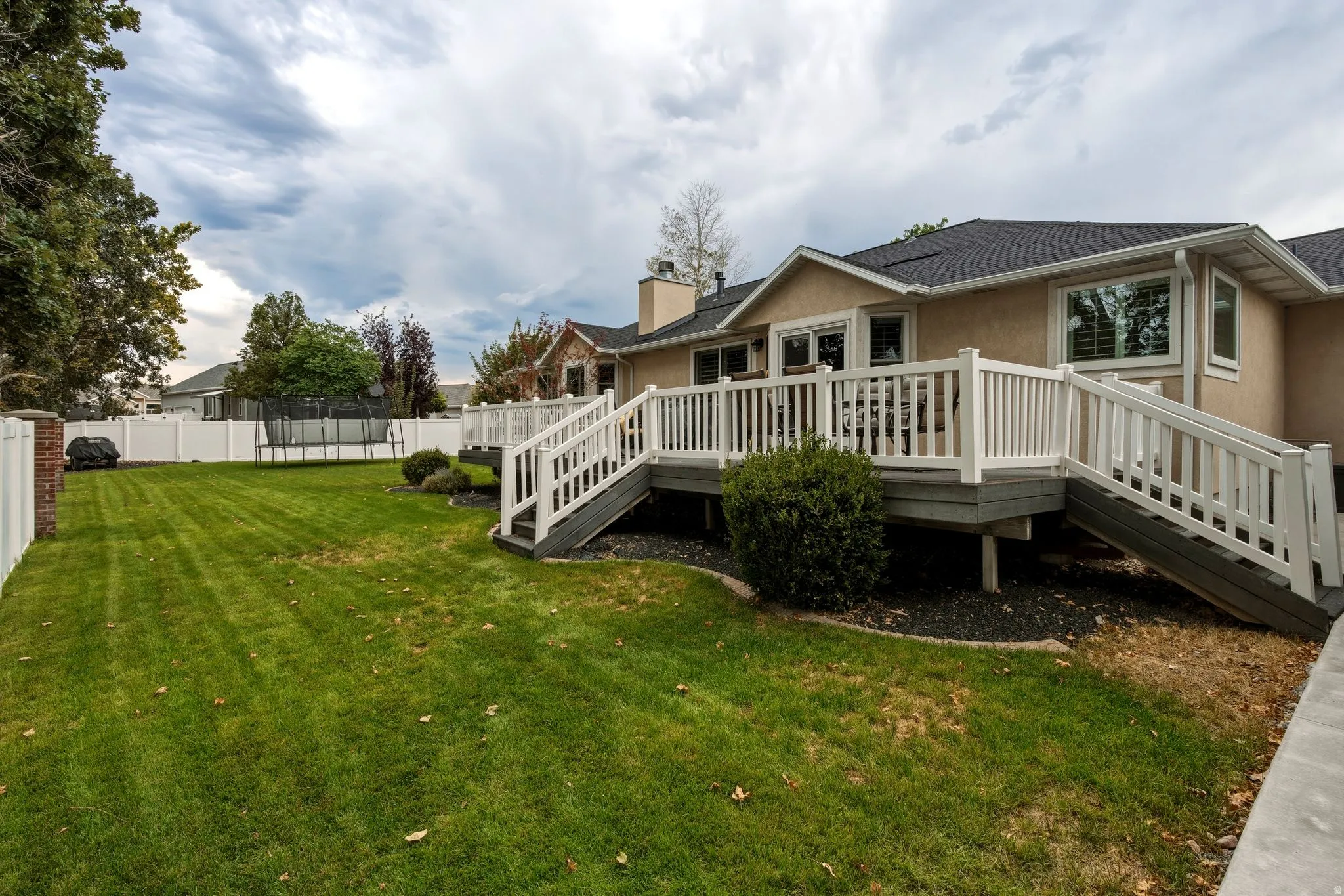 Spacious backyard with manicured lawn, mature landscaping, and white vinyl fencing