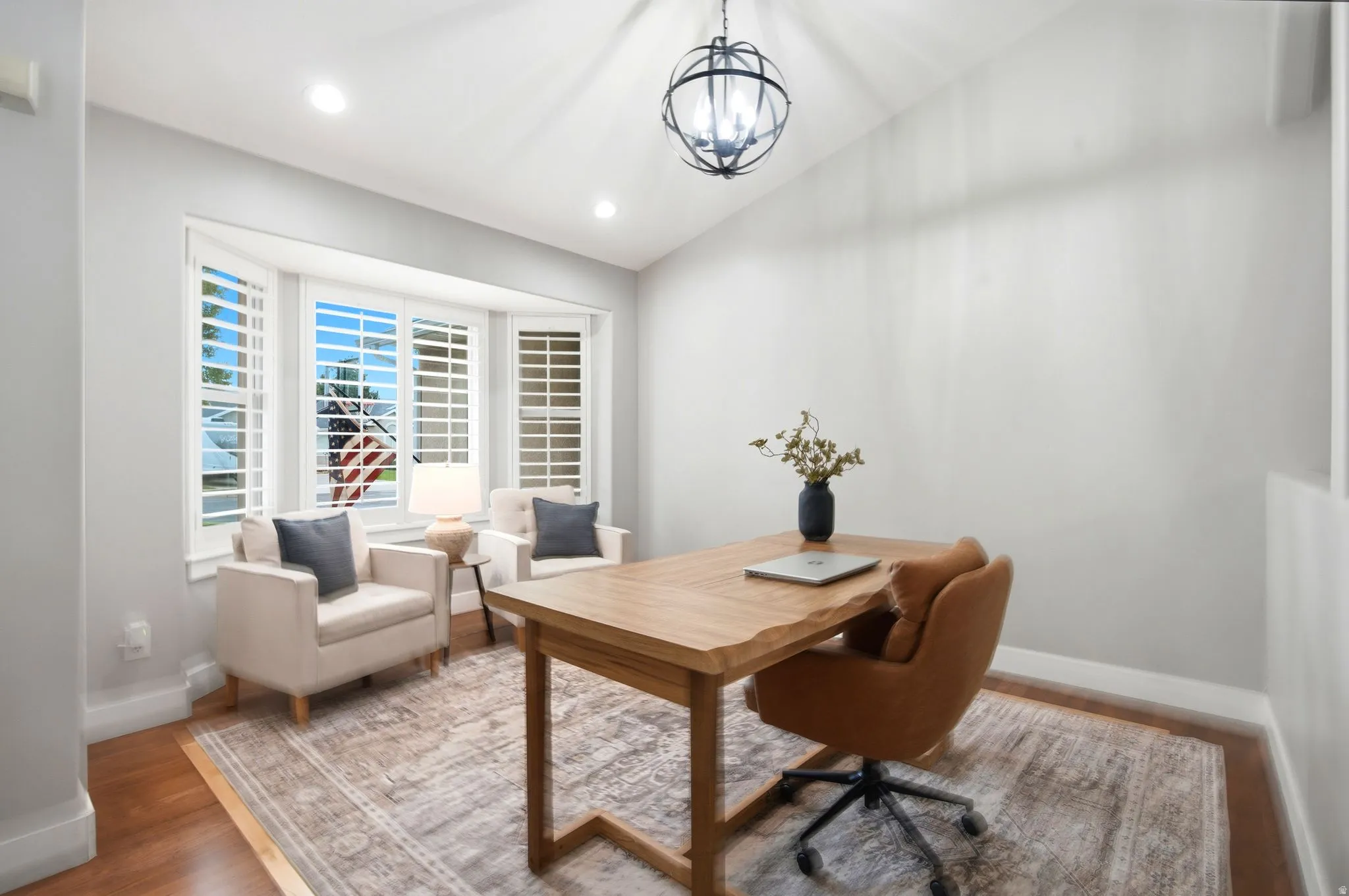Bright home office featuring hardwood flooring, a wood-top desk, pendant lighting, and abundant natural light from multi-pane windows with plantation shutters