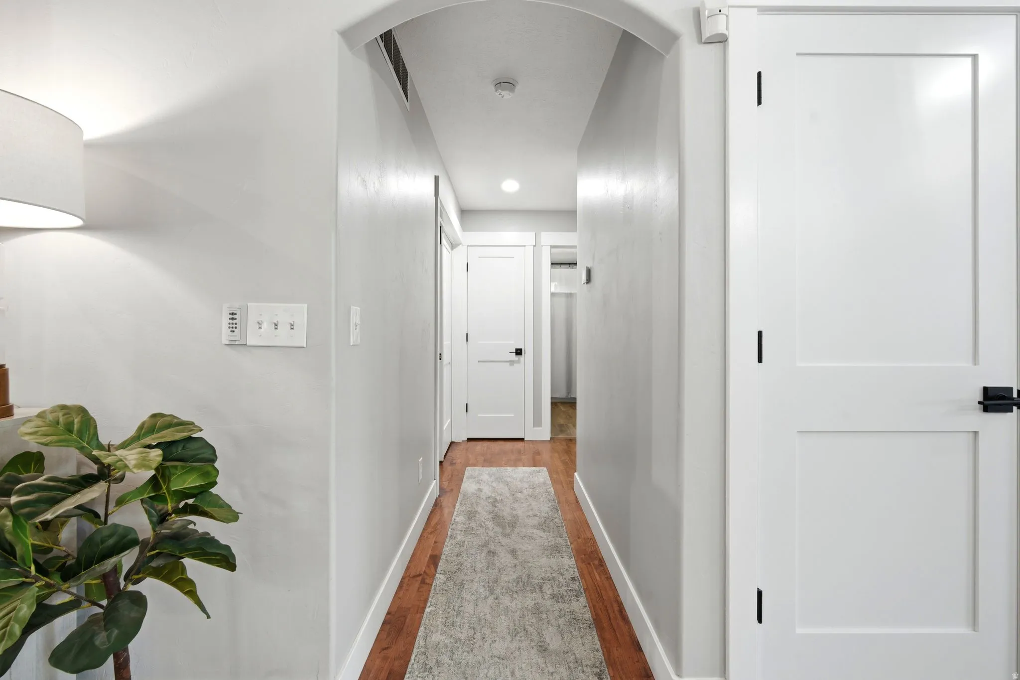 Hallway featuring recessed ceiling lighting, white painted walls, wood-finish flooring with gray runner, and white six-panel doors with black hardware throughout