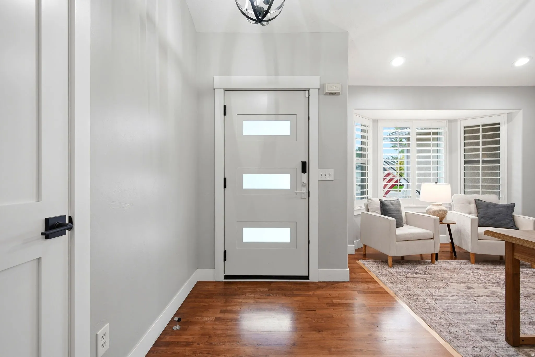 Hardwood flooring throughout, modern entry door with frosted glass panels, recessed lighting, and a bay window with plantation shutters