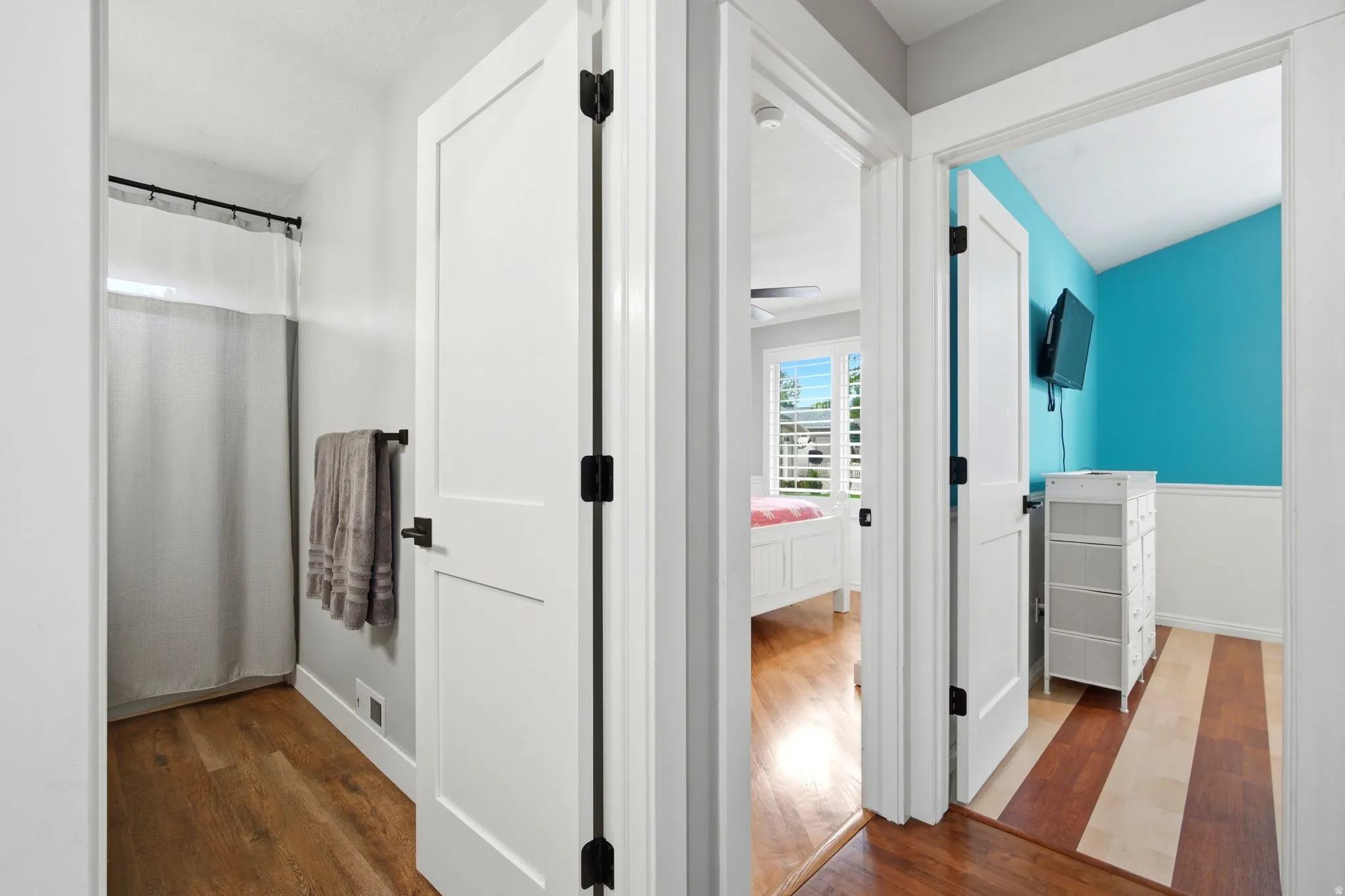 Bright hallway featuring wood-finish flooring, multiple white panel doors with black hardware, and accent wall painted in vibrant turquoise