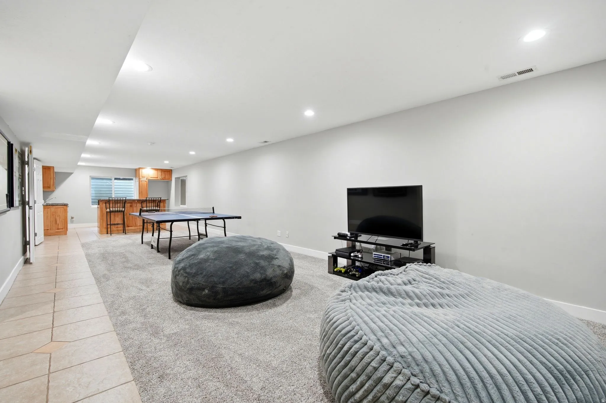 Expansive finished lower level featuring recessed lighting, a built-in wet bar with wood cabinetry, and tiled flooring