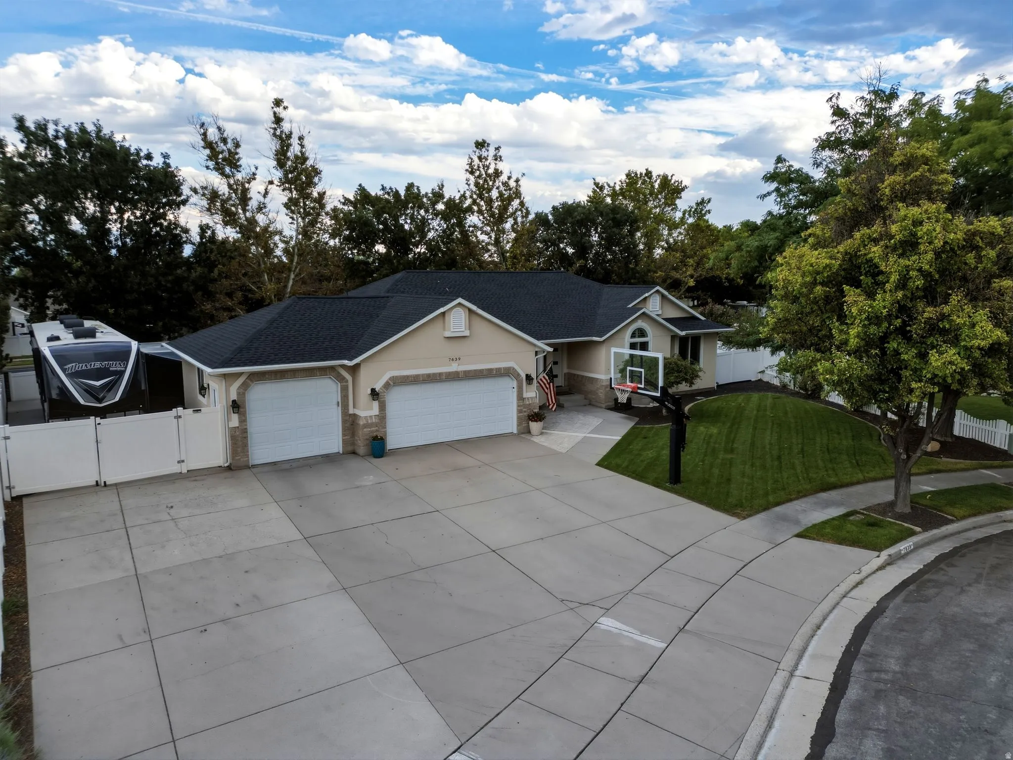 Elegant single-story residence featuring a three-car garage with white overhead doors, concrete driveway with geometric paving patterns, and a professionally manicured lawn with mature landscaping