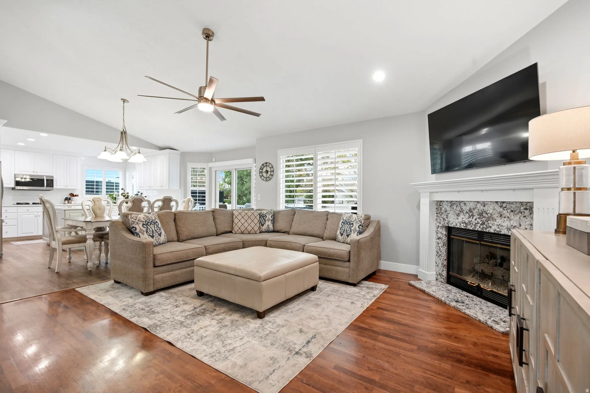 Open-concept living area featuring a spacious sectional arrangement anchored by a wood-burning fireplace with stone surround and white mantelpiece