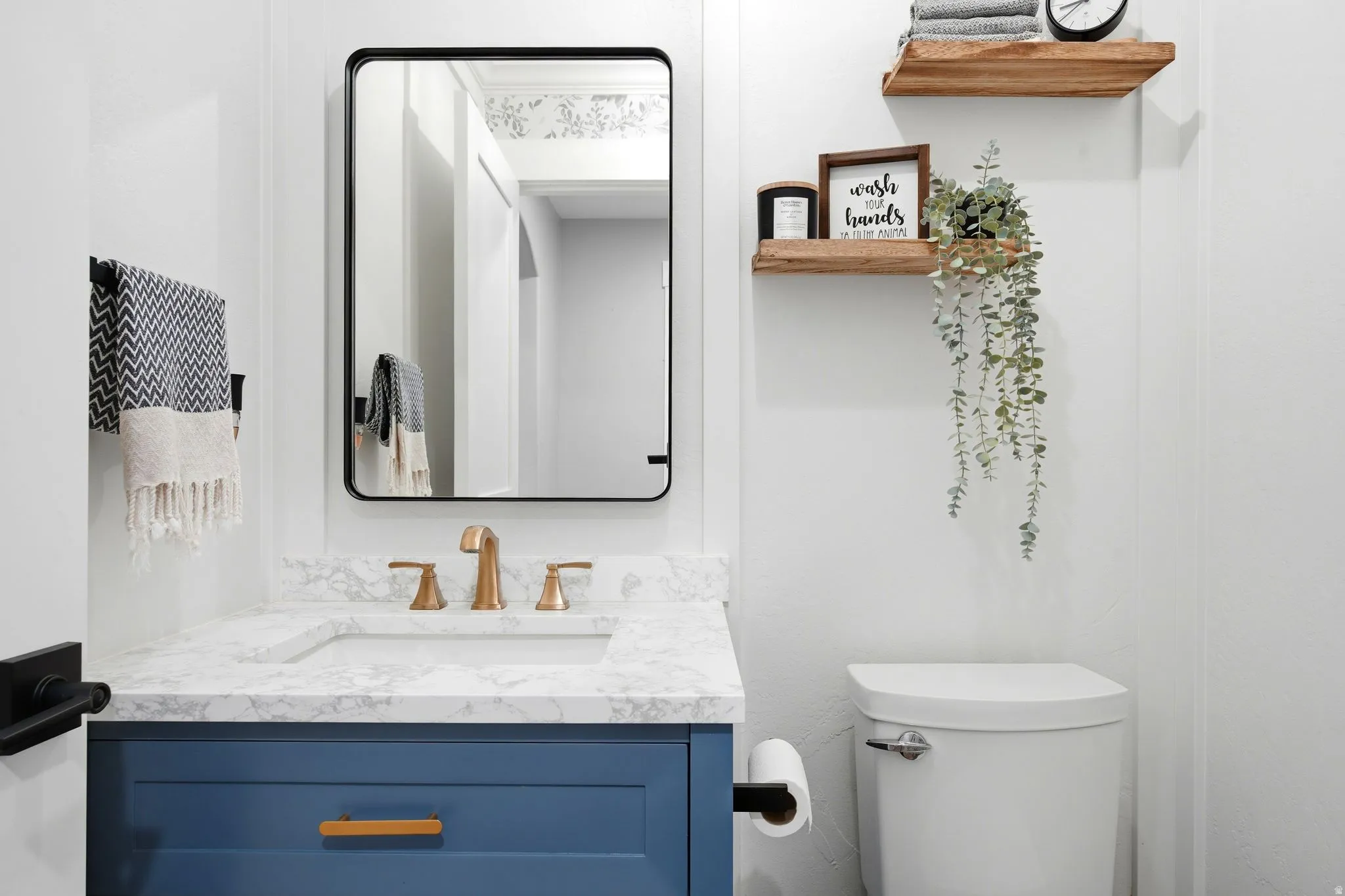 Modern bathroom featuring a navy blue vanity with brass hardware, white marble-look countertop, and integrated sink