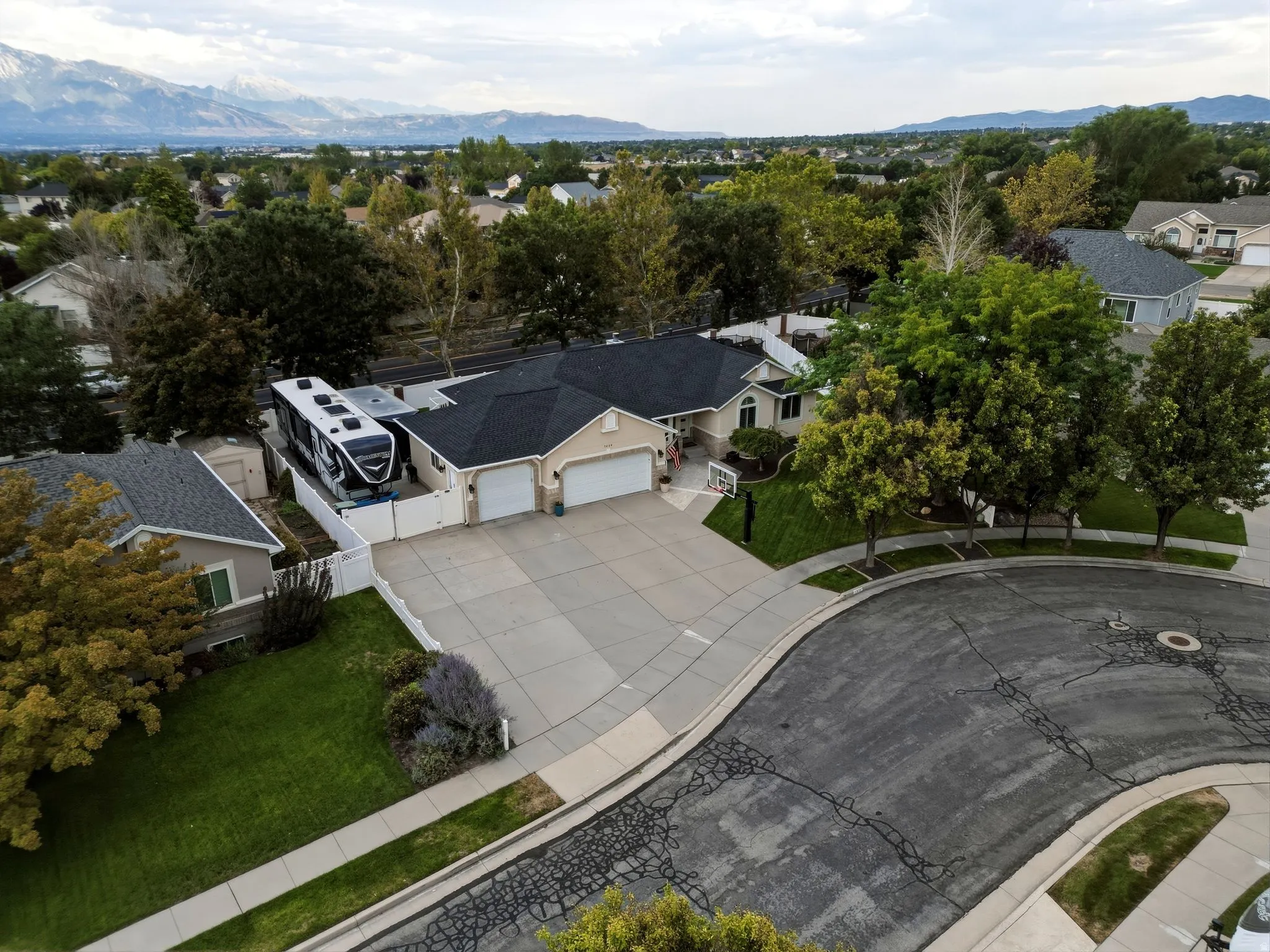 Stunning aerial perspective showcasing this contemporary residence featuring a dark architectural roof, expansive concrete driveway with circular design element, multiple garage bays, and mature landscaping throughout the property
