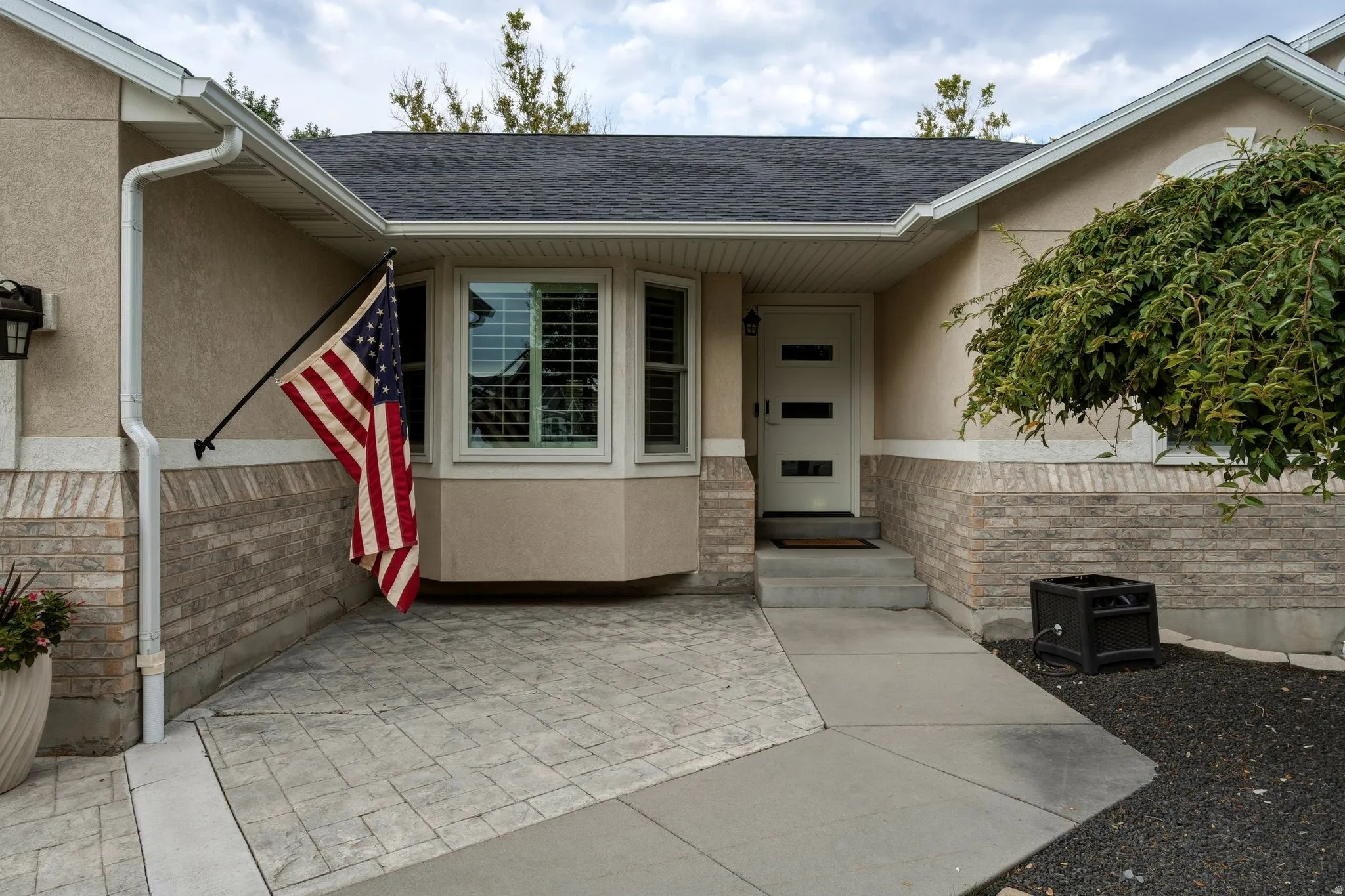 Welcoming front entry featuring a curved bay design with multi-pane windows, modern horizontal-panel entry door, and mixed-material facade combining stucco and stone veneer