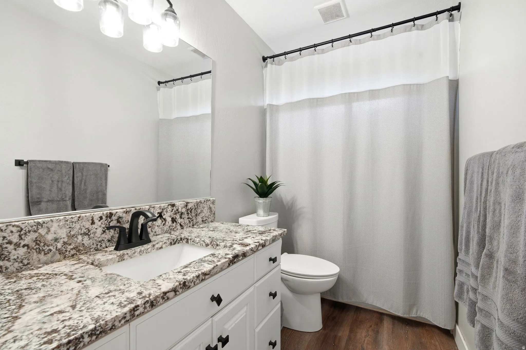 Spa-inspired bathroom showcasing a granite-topped double vanity with dual sinks, crisp white cabinetry with black hardware, and a ceramic toilet