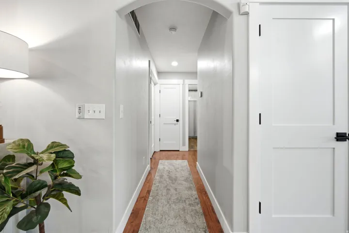 Hallway featuring recessed ceiling lighting, white painted walls, wood-finish flooring with gray runner, and white six-panel doors with black hardware throughout