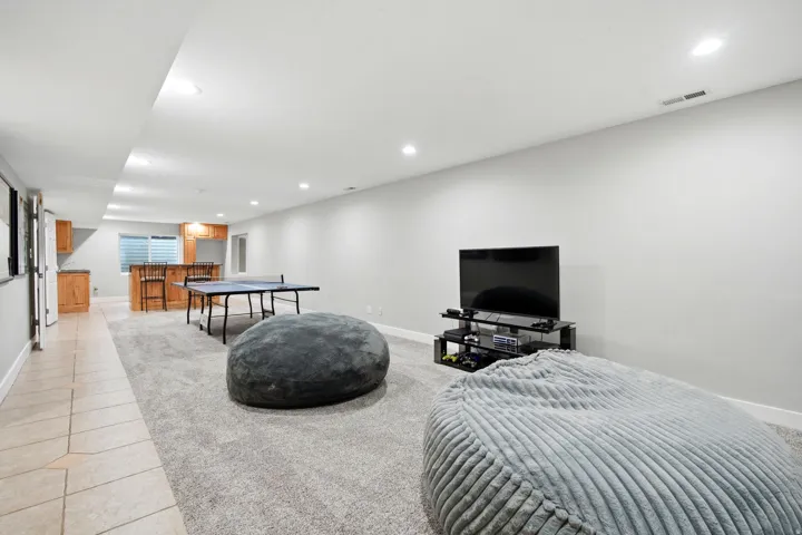 Expansive finished lower level featuring recessed lighting, a built-in wet bar with wood cabinetry, and tiled flooring