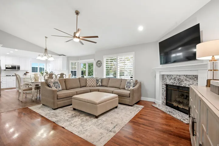 Open-concept living area featuring a spacious sectional arrangement anchored by a wood-burning fireplace with stone surround and white mantelpiece