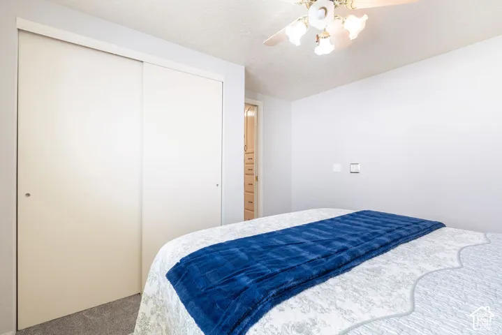 Room featuring neutral-toned carpeting, sliding closet doors, a multi-bulb ceiling fan, and built-in drawer cabinetry