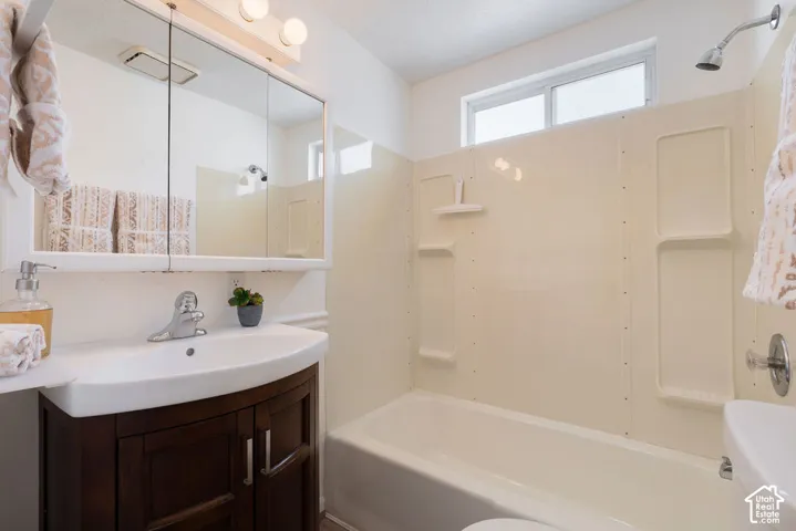 Bathroom featuring a vanity with dark wood-finish cabinetry, white basin, chrome single-handle faucet, integrated medicine cabinet with mirrored doors, and a tub-shower combination with built-in shelving