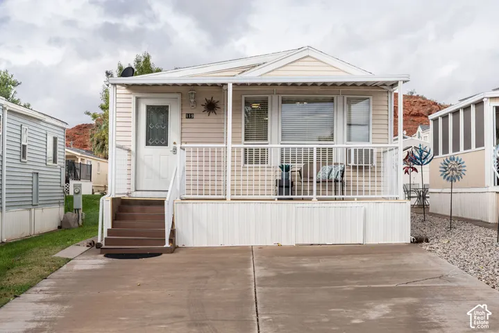 Exterior featuring light-toned horizontal siding, a covered front deck with white railings, stairs, and a concrete driveway