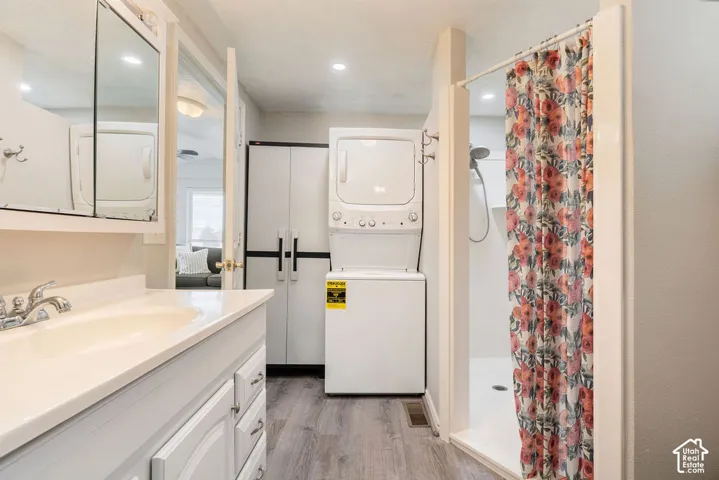 Bathroom featuring wood-finish flooring, white vanity cabinet with a integrated sink, recessed lighting, and a walk-in shower enclosure