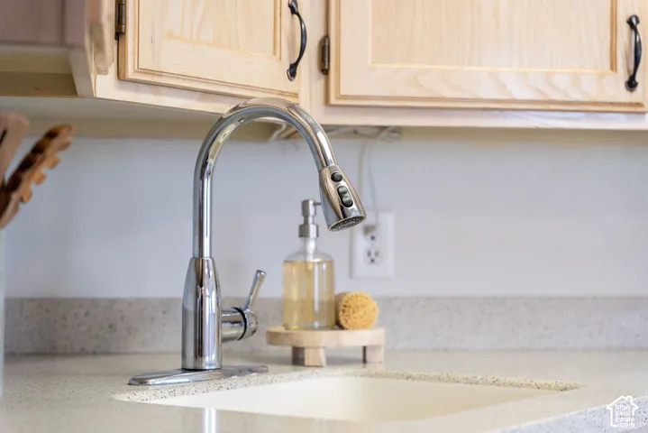 High-arc chrome faucet with pull-down sprayer, light wood-finish cabinetry with arched detailing, and solid-surface countertop with integrated backsplash
