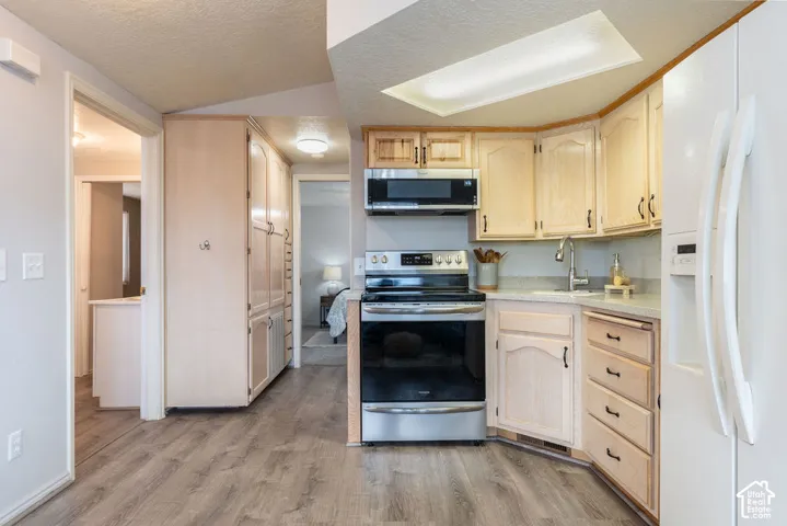 Kitchen featuring light wood-finish cabinetry, stainless steel appliances, wood-finish flooring, and a recessed ceiling light fixture