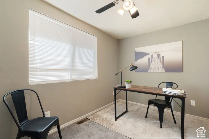 Neutral-toned interior space featuring a large window with horizontal blinds, carpeting, and a ceiling-mounted light fixture with a three-blade fan