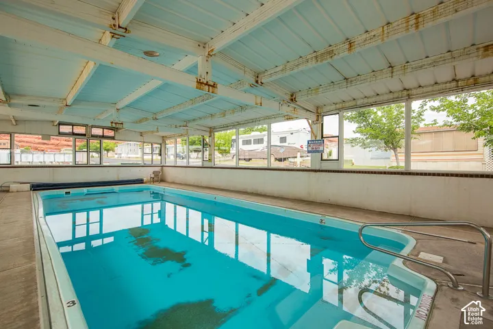 Indoor swimming pool with concrete decking, perimeter windows, and an exposed metal beam ceiling