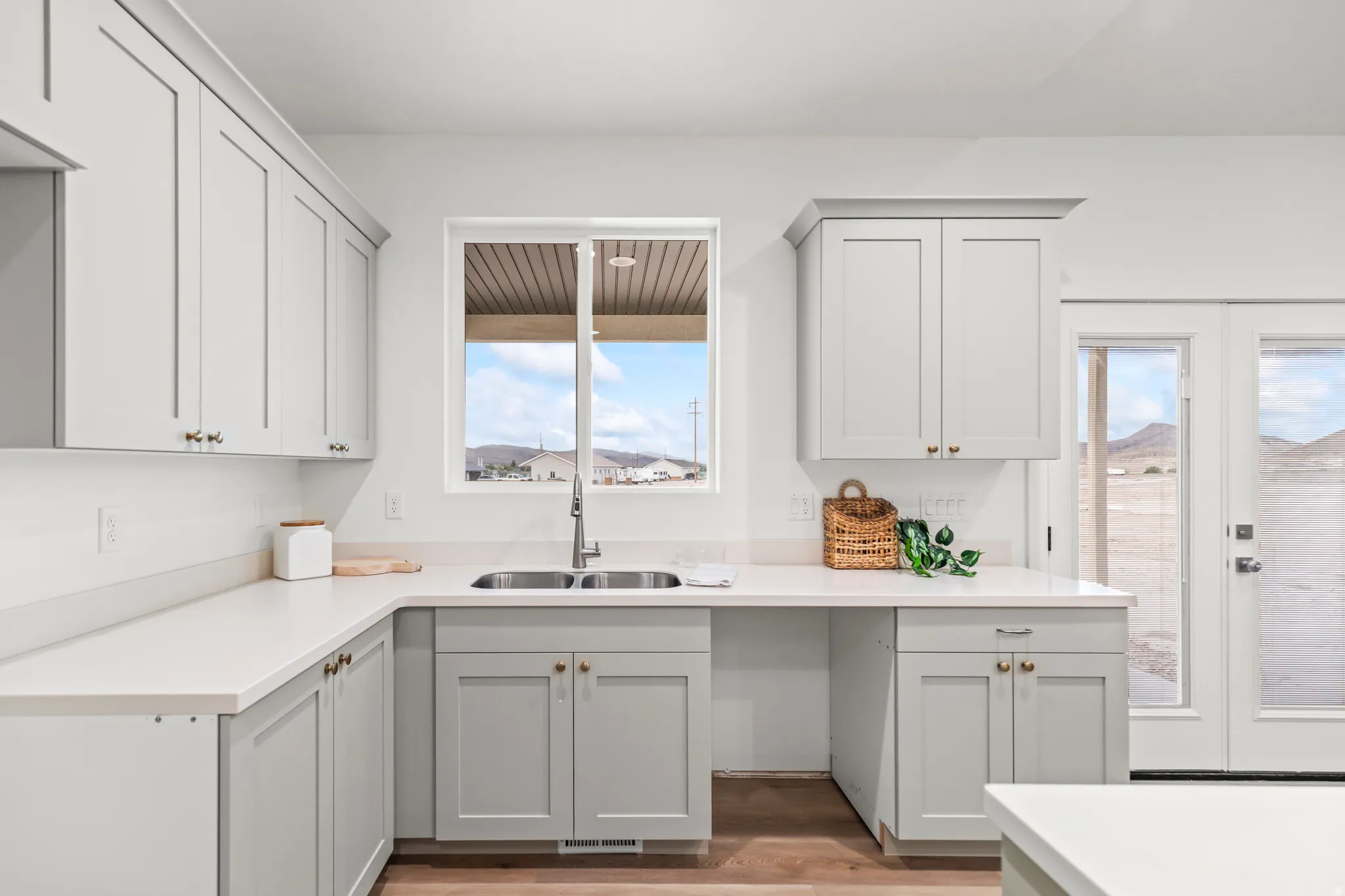 Light-toned cabinetry with gold-toned hardware, white solid-surface countertops, and a stainless steel double basin sink