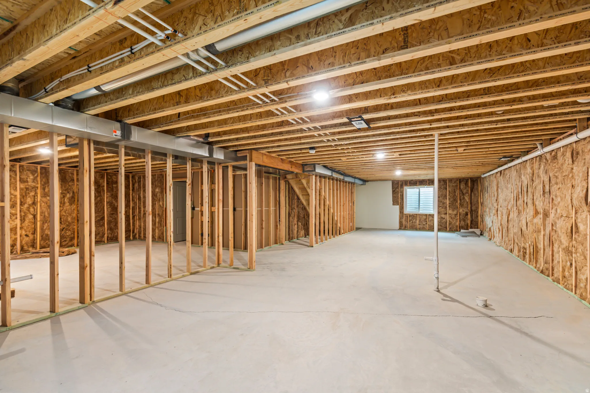 Unfinished basement with exposed ceiling joists, concrete flooring, framed wall partitions, and a window