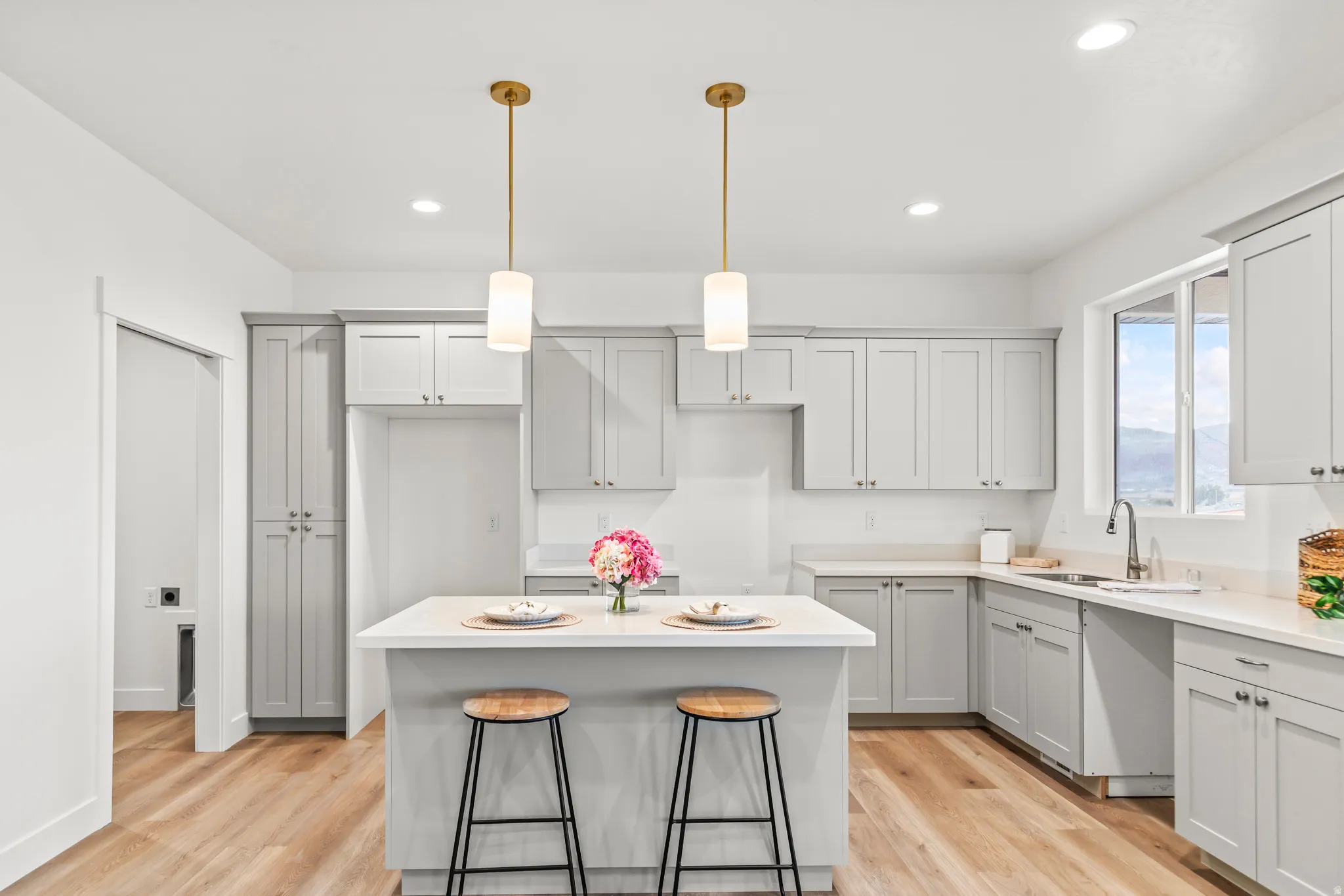 Spacious kitchen featuring an island with seating, light gray cabinetry, light countertops, wood-finish flooring, and two pendant lights