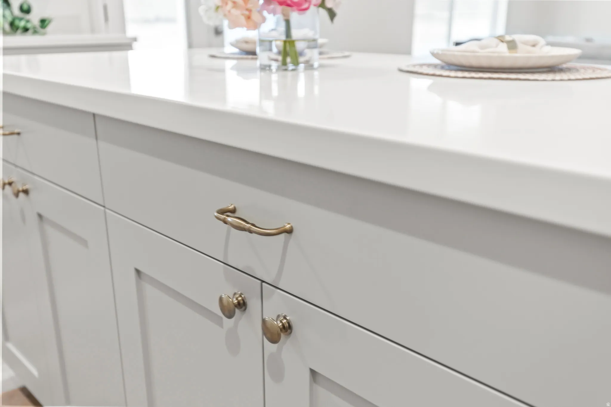 Smooth white countertop, light gray cabinetry, and decorative brass hardware