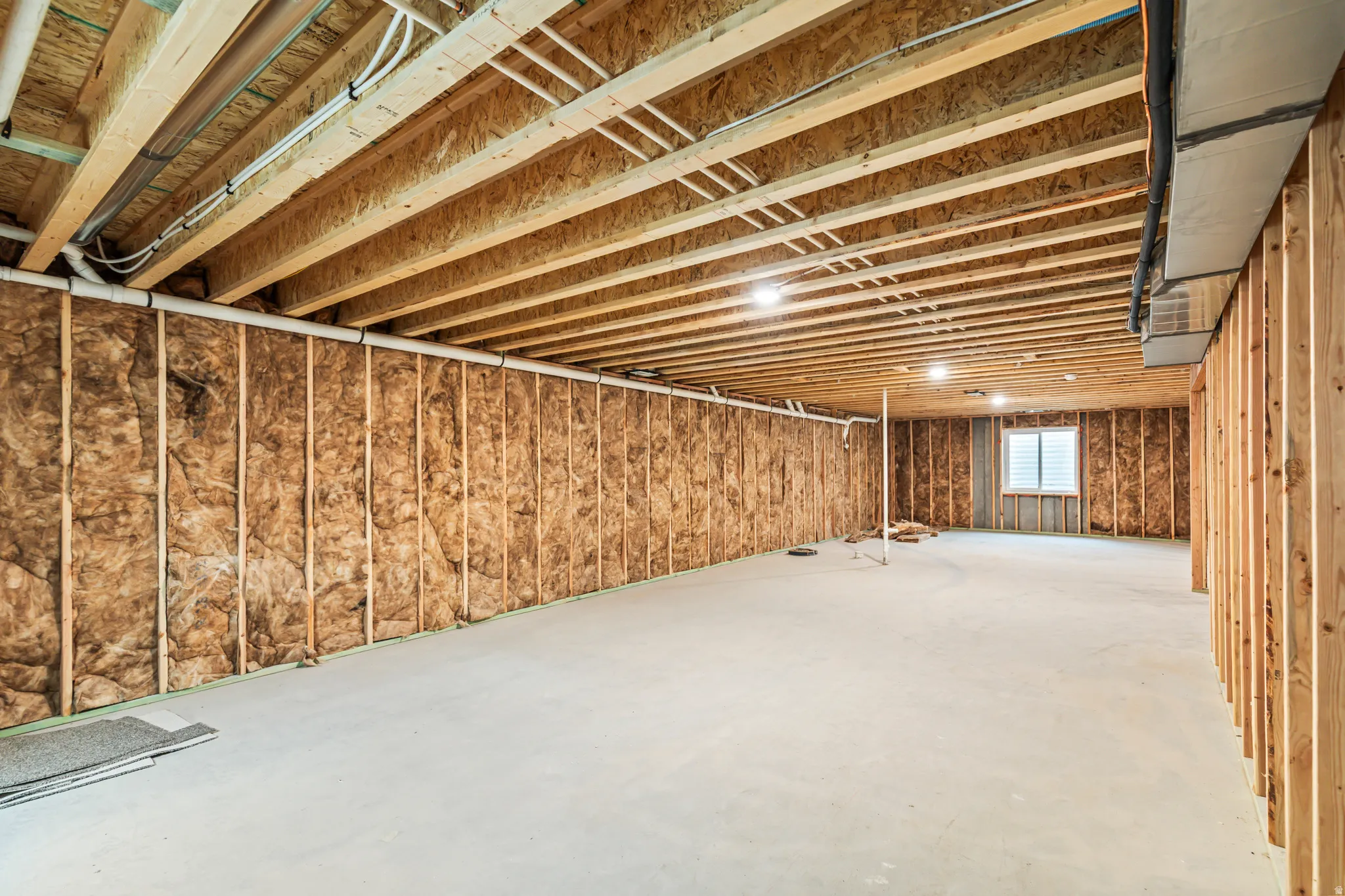 Unfinished basement with exposed ceiling joists, concrete flooring, and an egress window
