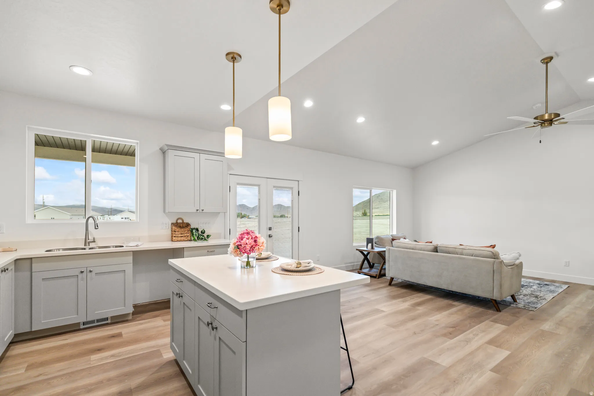 Open-concept living space with vaulted ceilings, recessed lighting, wood-finish flooring, a kitchen island with stone countertop, and light gray cabinetry