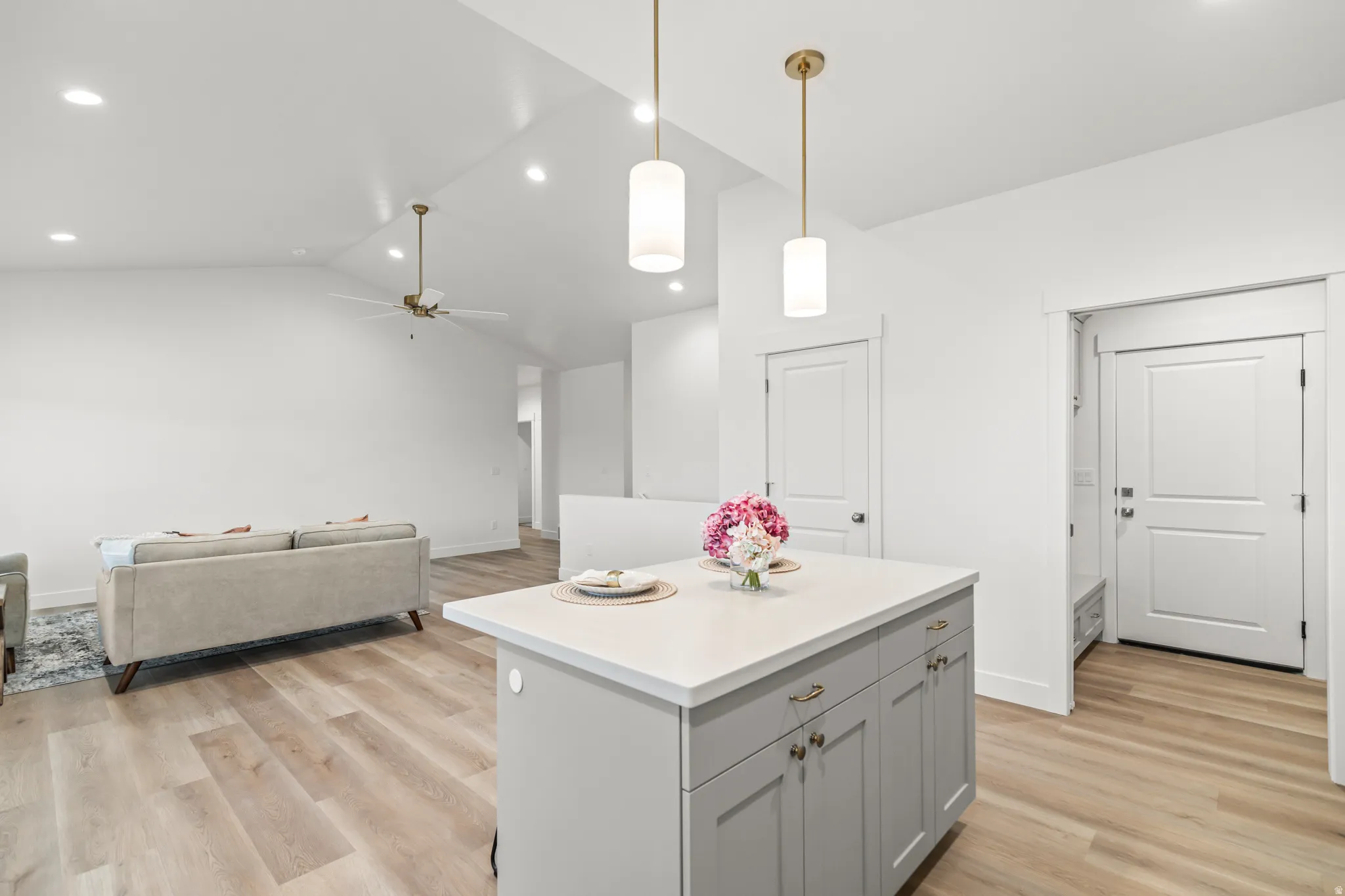 Kitchen island with a light-toned countertop, wood-finish flooring, recessed lighting, and vaulted ceilings